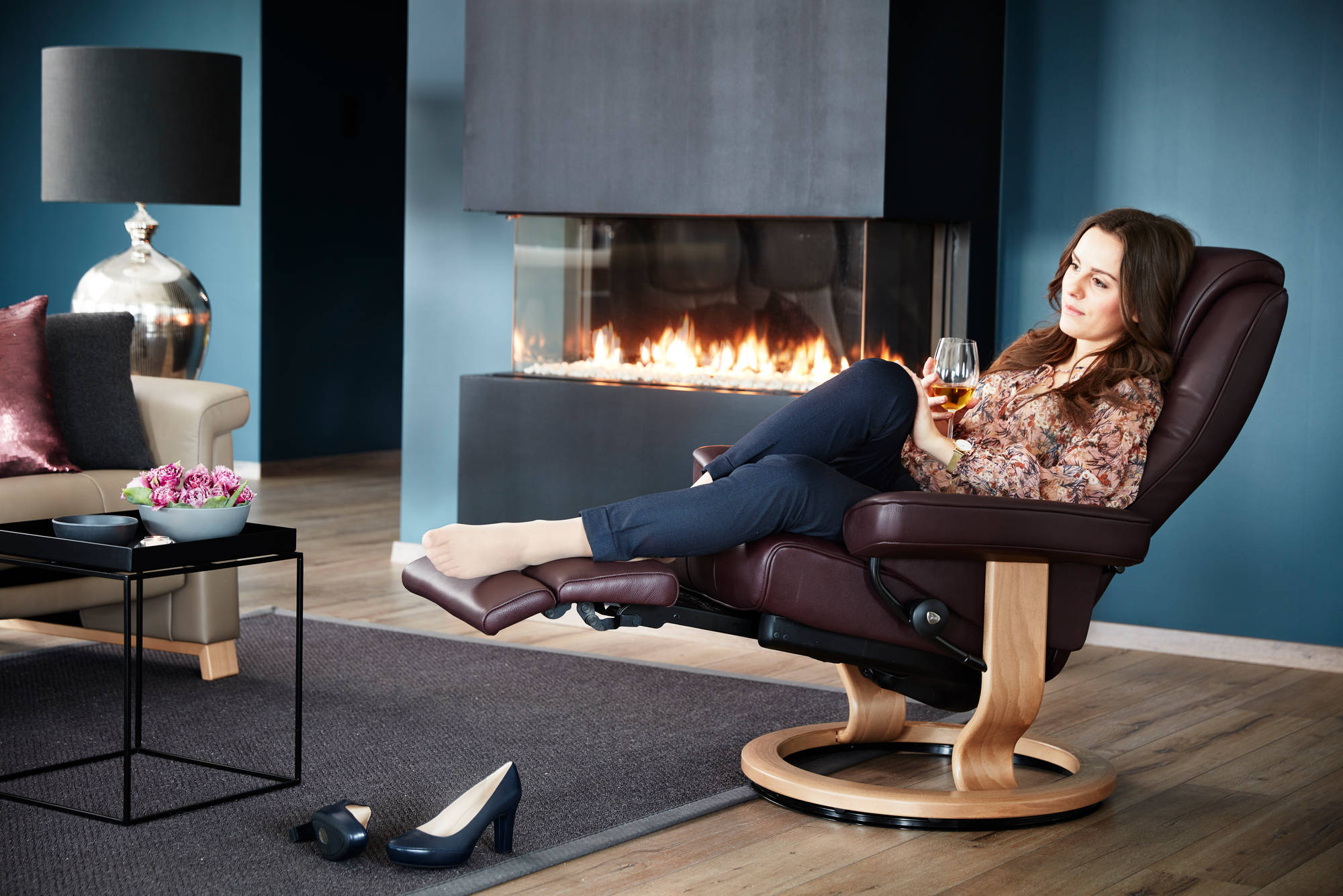 woman enjoying a glass of wine on a stressless recliner in front of a fireplace