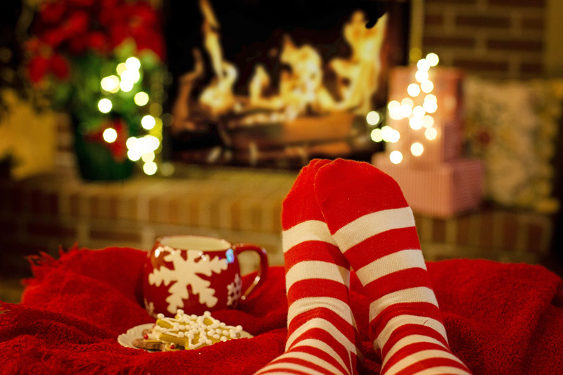 feet in cozy socks on an ottoman with a coffee mug and cookies nearby